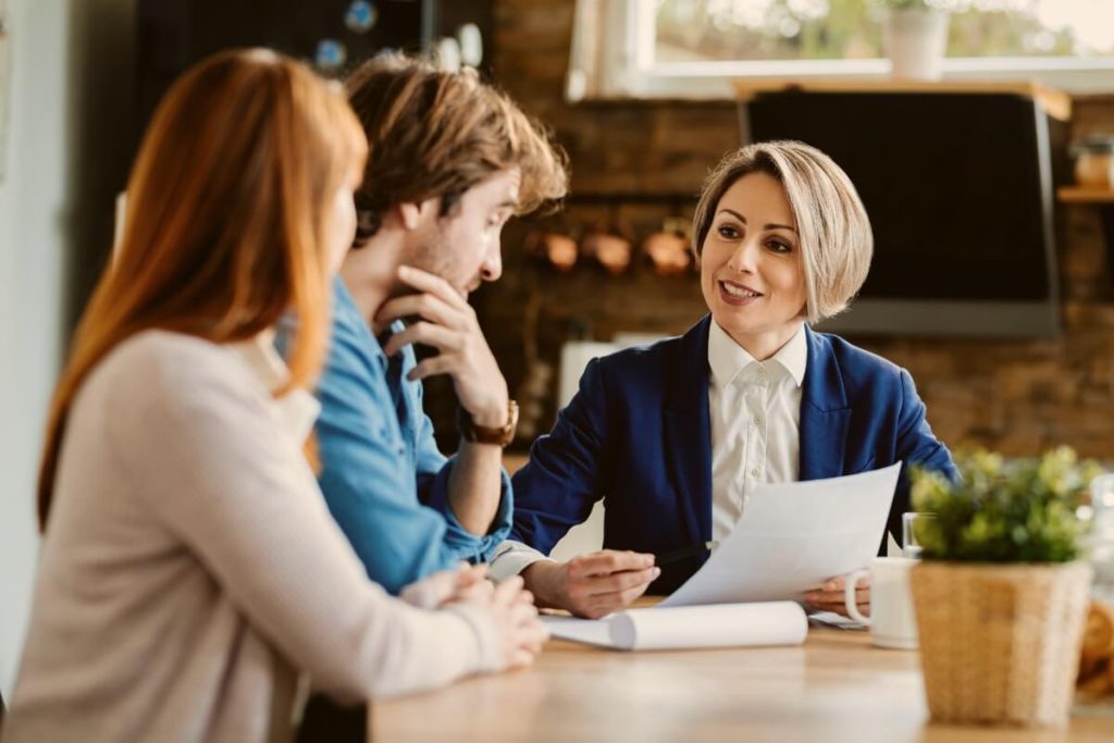Happy insurance agent talking to young couple about liability insurance at their home.